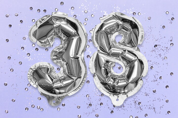 Silver foil balloon number, digit thirty eight on a lilac background with sequins. Birthday greeting card with inscription 38. Top view. Numerical digit. Celebration event, template.