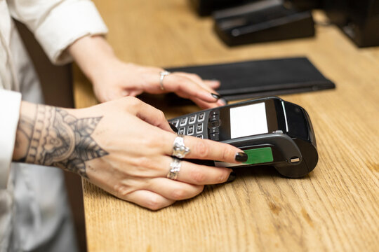 Young tattooed female cashier using credit card reader at checkout in bar