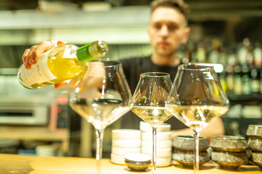 Male bartender pouring white wine in glasses at bar