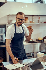 Male cafe owner holding pastry and writing in notebook