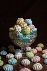 Glass with pile of colorful airy meringue cookies placed on table on brown background 