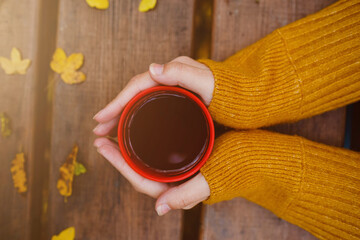 cup of hot tea in female hands holding it on wooden table autumn background with leaves. Warm drink concept.