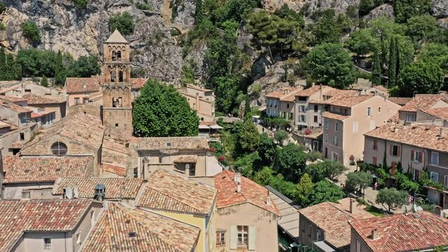 Moustiers Sainte Marie France Aerial v4 drone low reverse flyover medieval village town located at the foot of steep rock cut by a small ravine - July 2021