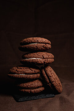 Pile of chocolate sandwich cookies with white cream filling stacked on slate board on table on brown background 