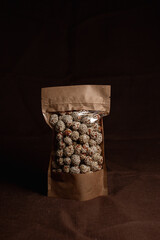 Sweet nuts glazed in sugar and covered with sesame seeds packed in paper bag and placed on brown background in dark studio 