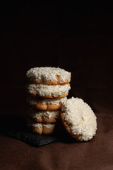 Stack of cookies with coconut flakes placed on slate board on table in studio with brown background 