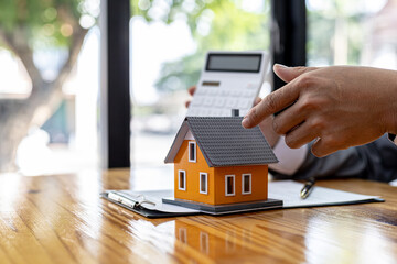 Man holding a calculator and pointing a model of a house on a table, a salesperson showing numbers...