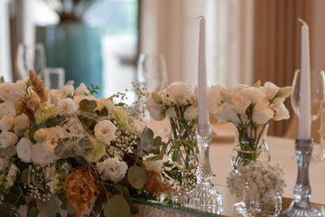 White tablecloths with clear vases and white flowers and fern arrangements. Golden colored plates, peavh napkins, table numbers and mirror centerpieces.