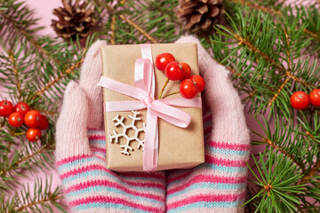 A girl in mittens holds a Christmas gift box on a background of fir branches and cones
