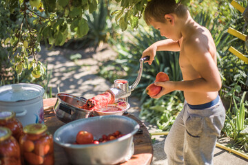 Making homemade tomato  juice  pressing in a hand press with a screw children help to turn the...