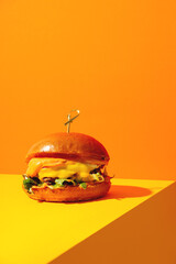 Big burger with cheese on bright orange and yellow background. American Fast food cuisine in a modern style. - obrazy, fototapety, plakaty
