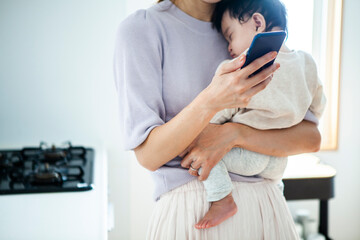 赤ちゃんを抱きながらスマートフォンを操作する女性
