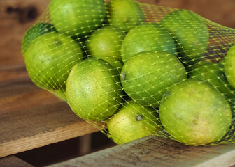 Macro of fresh limes in a net on a wooden board