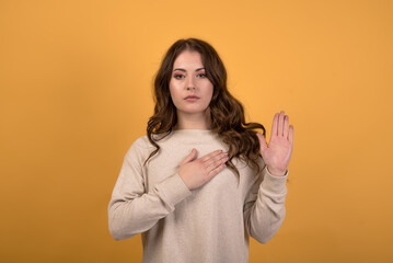 Attractive and happy caucasian brunette girl with wavy hair in a casual jumper holding her hand on...