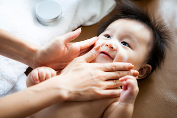 赤ちゃんの肌に保湿クリームを塗る母親