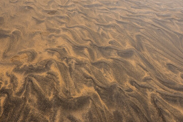 Amazing natural sand pattern made by wind and water on a sandy beach. Unique design for creative purpose. Design background. Random shapes on a dark and light sand surface