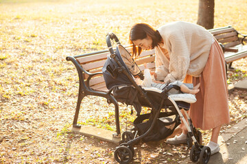 秋の公園・ベビーカーに乗った赤ちゃんをあやすお母さん