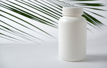 Mockup. White plastic bottle for vitamins, cosmetics, health care products on a white background with green palm leaves. Cosmetic medical beauty product