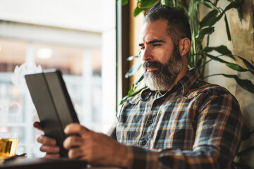 Adult man is sitting in cafe and using digital tablet.