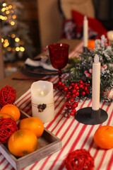 Festive decoration of the New Year's table, serving dishes for New Year's dinner, cones, tangerines, fir branches, garlands, candles and glasses, bokeh on the background. The concept of Christmas