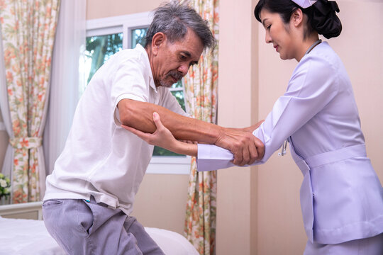 Young nurse helping elderly man stand up from bed.