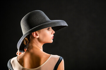 Portrait of a beautiful young girl in an elegant black hat on a black background
