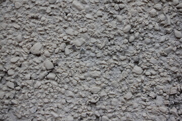 Rough grey dry concrete wall surface interspersed with crushed stone close up industrial background texture