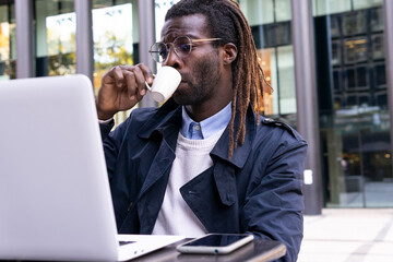 Black freelancer drinking coffee while working on laptop