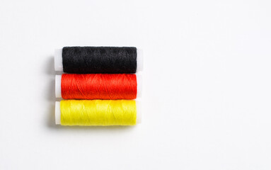 Three multi-colored spools of thread for sewing are stacked in the form of the flag of Germany on a white background. There is a free empty space.