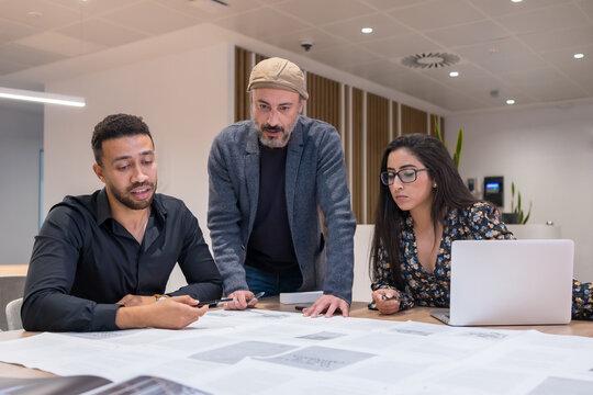 Diverse Colleagues Discussing Project Documentation In Workspace With Papers