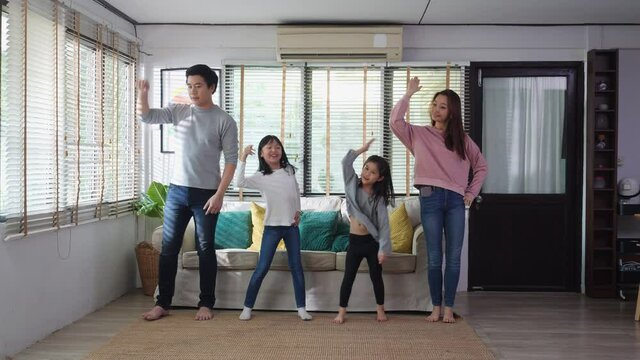 Asian family dancing together in living room at home. Father, mother and daughter enjoyment with music while being celebration at home. Leisure activity stay at home of happy family.