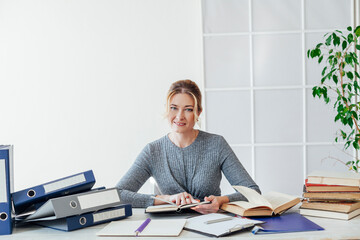 a business woman in a suit sits at an office desk with books