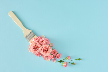 Creative spring concept with pink roses and paint brush on pastel blue background. Flowers composition, flat lay, copy space. Nature bloom idea.