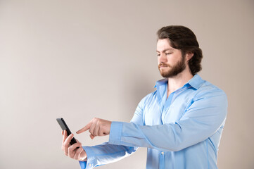 Serious bearded man wearing blue shirt  using smartphone isolated on grey background