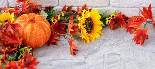 banner with beautiful autumn still life with sunflowers, red- yellow flowers, autumn leaves and orange pumpkin on white brick wall background. front view.