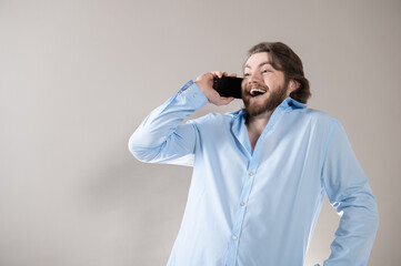 Young bearded man having call and talking on smartphone with pleasure isolated over grey background