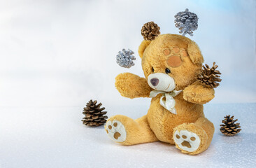 A teddy bear juggles New Year's cones on a light blue background. Selective focus