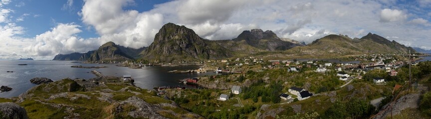 Fototapeta na wymiar panorama of sunny day at reine Lofoten islands norway with blue sky and tiny clouds, fishermen village with huge mountains in a fjord