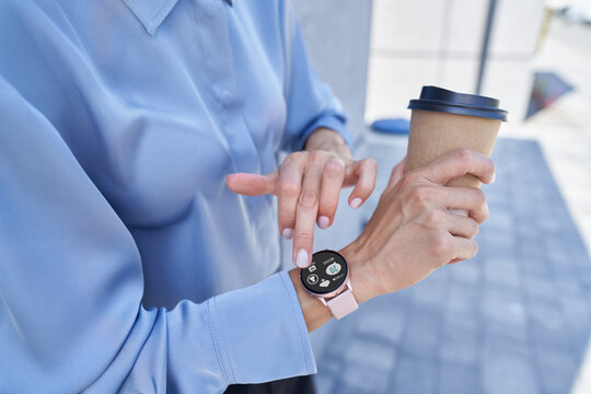 Businesswoman holding disposable coffee cup while using smart wristwatch