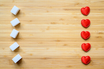 Sugar cubes and hearts on a wooden board. There is an empty space in the center. Diabetes protection concept.