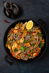 Wheat noodles with black sesame, fried in a wok with chicken and vegetables. Top view.