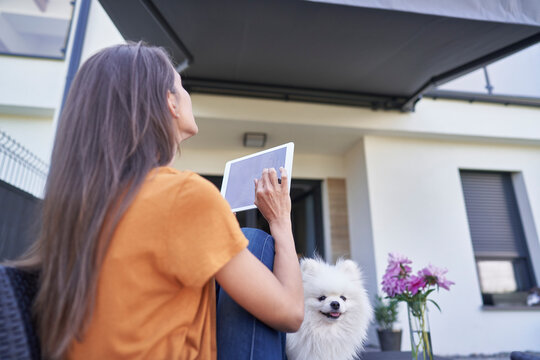 Woman opening awning outside house through digital tablet