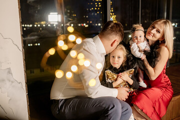 Young beautiful family with two daughters in smart clothes are hugging in the living room, celebrating the christmas holiday