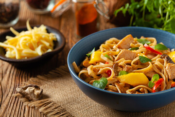 Fried chicken with mango and coconut milk with noodles. Prepared in a wok. Front view. Served in a blue bowl.