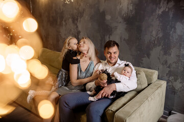 Naklejka premium Young beautiful family with two daughters in smart clothes are hugging in the living room, celebrating the christmas holiday