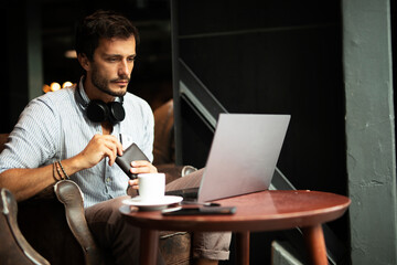 Businessman working on laptop and sitting in cafe. Young man holding credit card...