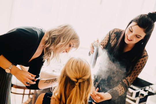 Female hairdresser spraying hairspray on bride while standing by make-up artist