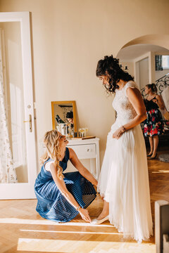 Smiling bridesmaid helping bride with wearing shoe