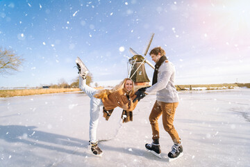 Loving couple having fun on ice in typical dutch landscape with windmill. Woman and man ice skating...