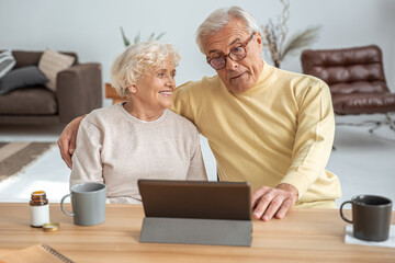 Mature spouses embracing while looking at the tablet with pleasure smiles